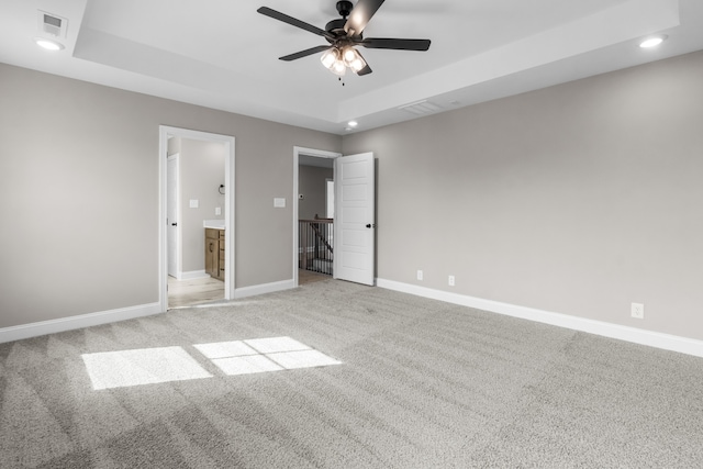 unfurnished bedroom featuring ensuite bathroom, light colored carpet, ceiling fan, and a raised ceiling