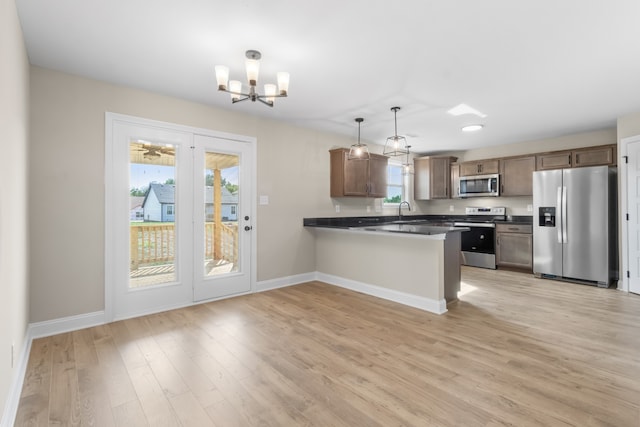 kitchen featuring stainless steel appliances, decorative light fixtures, an inviting chandelier, light hardwood / wood-style floors, and kitchen peninsula