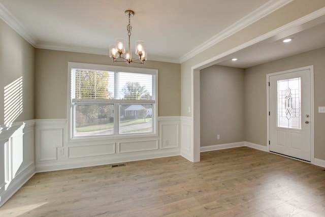 unfurnished dining area with light wood-type flooring, a chandelier, and ornamental molding