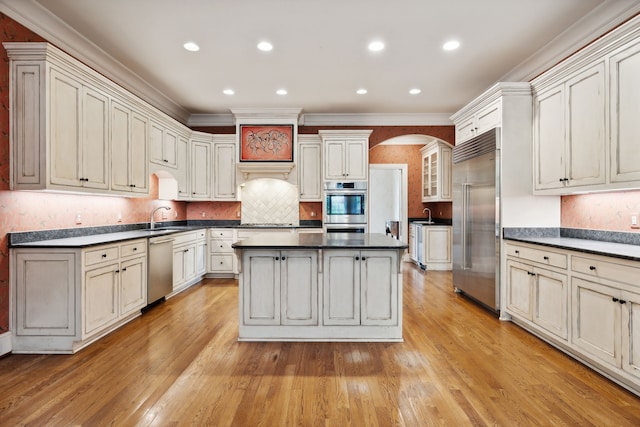 kitchen featuring tasteful backsplash, a kitchen island, sink, light wood-type flooring, and appliances with stainless steel finishes