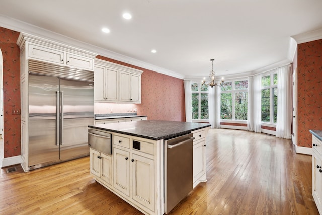 kitchen featuring hanging light fixtures, appliances with stainless steel finishes, a center island, and ornamental molding