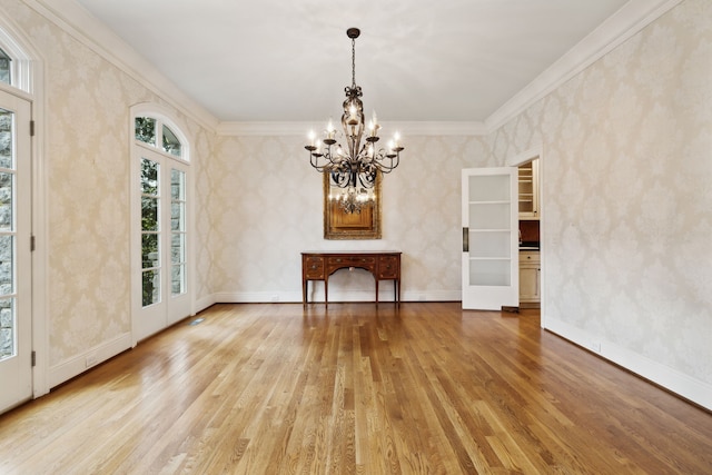 unfurnished dining area with french doors, an inviting chandelier, crown molding, and light hardwood / wood-style flooring