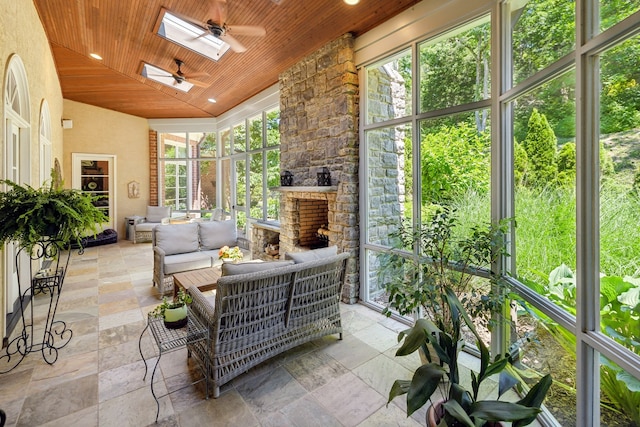 sunroom / solarium featuring ceiling fan, wood ceiling, a stone fireplace, and lofted ceiling with skylight