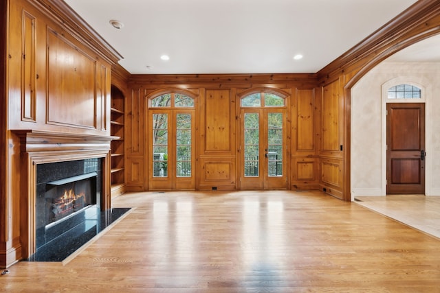 unfurnished living room featuring wood walls, a wealth of natural light, light wood-type flooring, built in features, and french doors