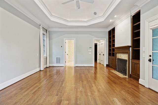 unfurnished living room with crown molding, built in features, a tray ceiling, and light hardwood / wood-style flooring