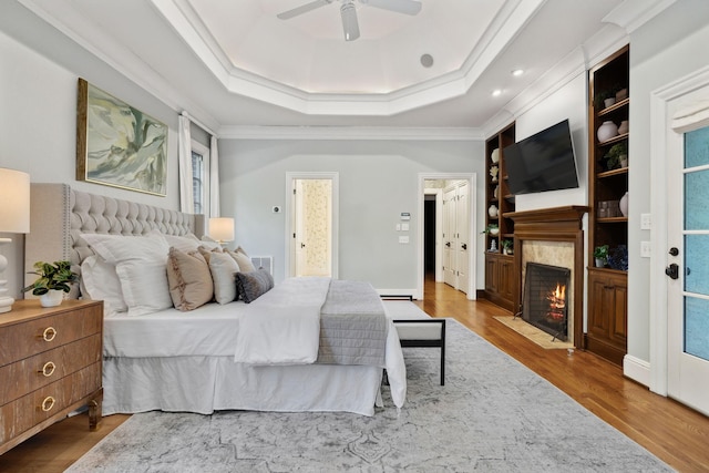 bedroom with connected bathroom, ornamental molding, ceiling fan, a tray ceiling, and light hardwood / wood-style flooring