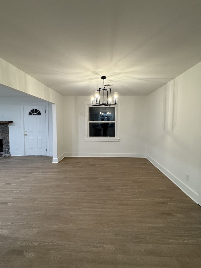 unfurnished dining area featuring dark hardwood / wood-style flooring, a stone fireplace, and a notable chandelier