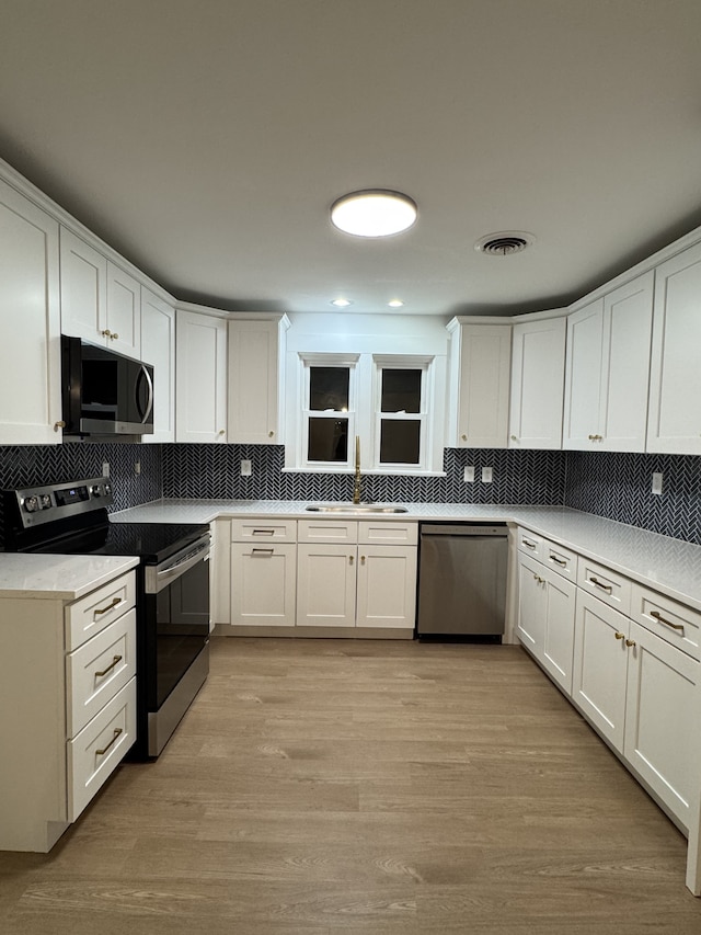 kitchen with white cabinetry, light hardwood / wood-style floors, appliances with stainless steel finishes, and sink