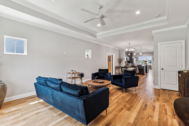 living room featuring a tray ceiling, ceiling fan with notable chandelier, crown molding, and light hardwood / wood-style flooring