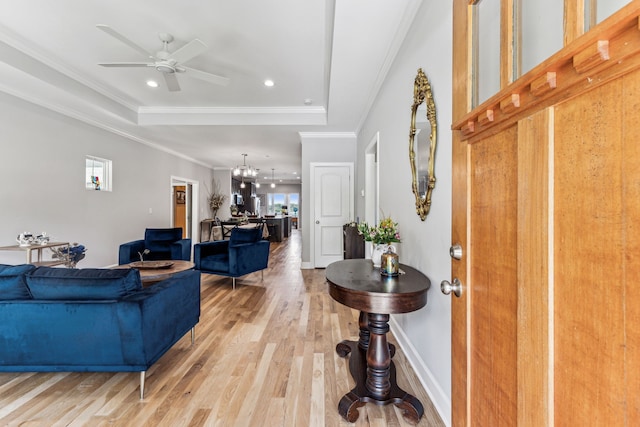 living room featuring light hardwood / wood-style floors, ceiling fan with notable chandelier, a raised ceiling, and crown molding