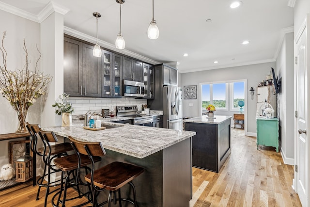 kitchen featuring light hardwood / wood-style floors, a center island, hanging light fixtures, a breakfast bar area, and appliances with stainless steel finishes