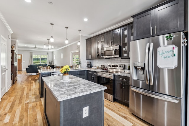 kitchen featuring stainless steel appliances, pendant lighting, light wood-type flooring, and ornamental molding