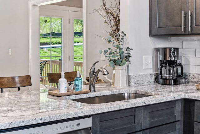 kitchen featuring light stone counters, dishwasher, sink, tasteful backsplash, and dark brown cabinets