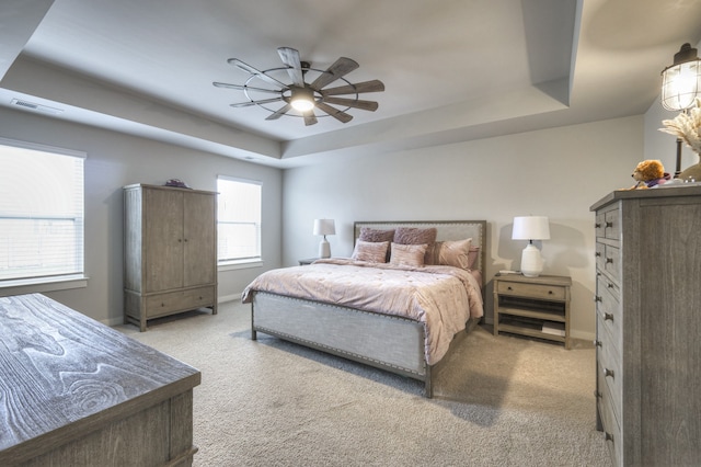 bedroom with light colored carpet, ceiling fan, and a tray ceiling