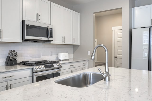 kitchen featuring stainless steel appliances, white cabinetry, sink, light stone countertops, and backsplash