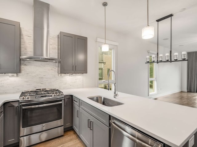 kitchen featuring sink, kitchen peninsula, appliances with stainless steel finishes, wall chimney exhaust hood, and decorative light fixtures