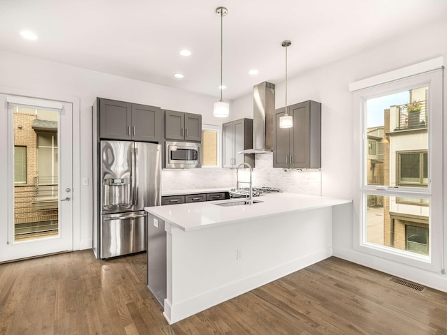 kitchen featuring appliances with stainless steel finishes, wall chimney range hood, gray cabinetry, a peninsula, and recessed lighting