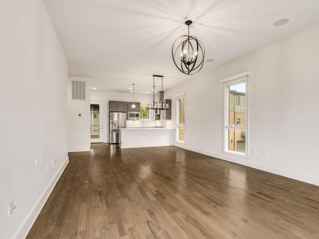 unfurnished living room with a chandelier, dark wood finished floors, and baseboards