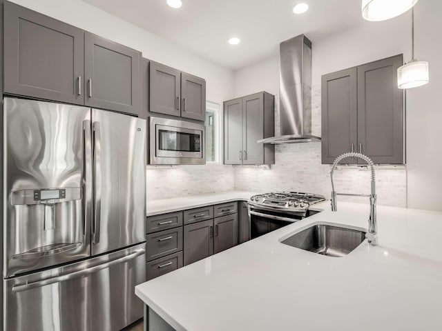 kitchen with stainless steel appliances, wall chimney range hood, a sink, light countertops, and gray cabinets