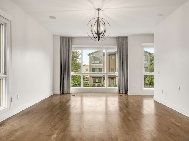 unfurnished dining area featuring dark wood-type flooring, a healthy amount of sunlight, and an inviting chandelier