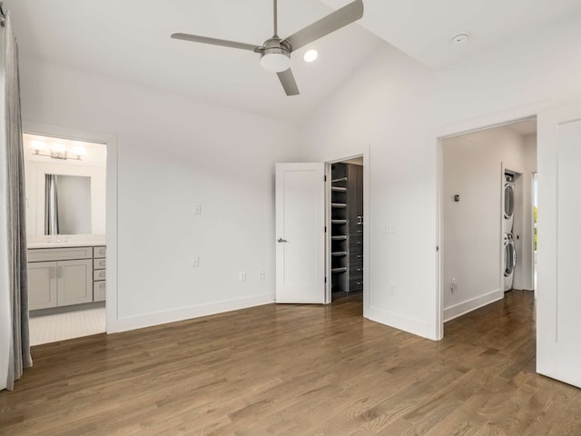 unfurnished bedroom with ensuite bathroom, ceiling fan, a spacious closet, stacked washing maching and dryer, and dark wood-type flooring