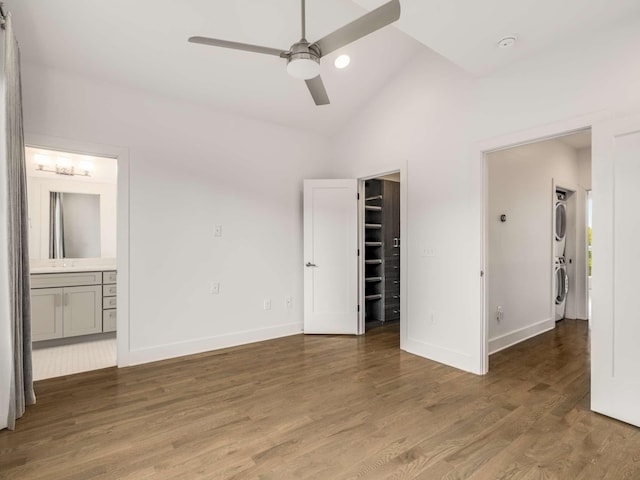 unfurnished bedroom featuring stacked washer and clothes dryer, baseboards, a walk in closet, wood finished floors, and ensuite bath