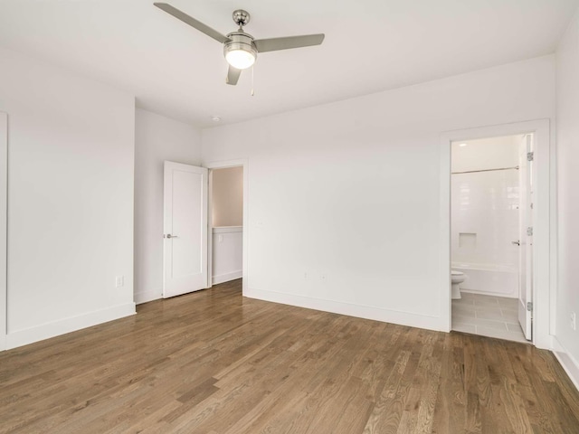 unfurnished bedroom featuring wood finished floors, ensuite bathroom, baseboards, and ceiling fan