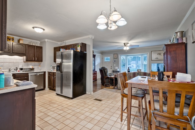 kitchen featuring ceiling fan with notable chandelier, dark brown cabinetry, ornamental molding, backsplash, and appliances with stainless steel finishes