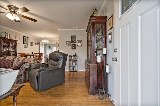 living room featuring light wood-type flooring, ceiling fan with notable chandelier, and crown molding