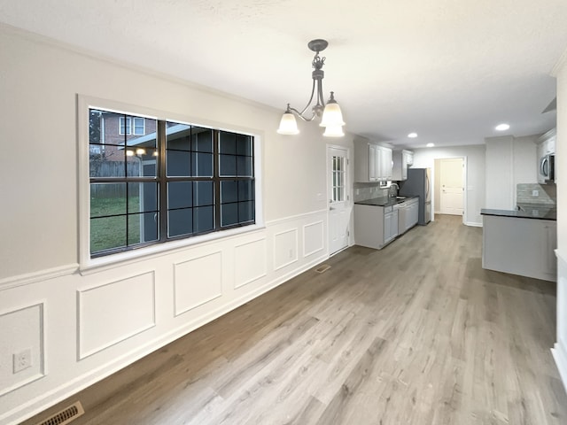 kitchen with white cabinetry, appliances with stainless steel finishes, light wood-type flooring, a notable chandelier, and hanging light fixtures