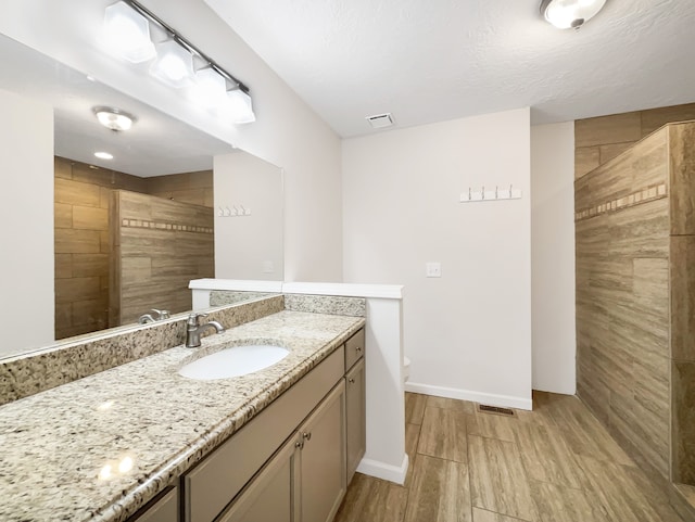 bathroom with toilet, hardwood / wood-style floors, a textured ceiling, a tile shower, and vanity