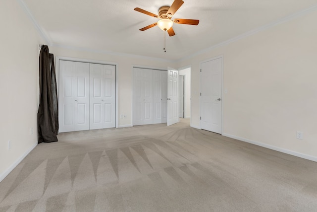 unfurnished bedroom with ceiling fan, light colored carpet, two closets, and ornamental molding