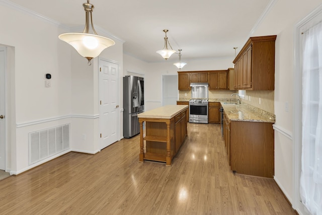 kitchen with sink, light hardwood / wood-style flooring, ornamental molding, a kitchen island, and stainless steel appliances