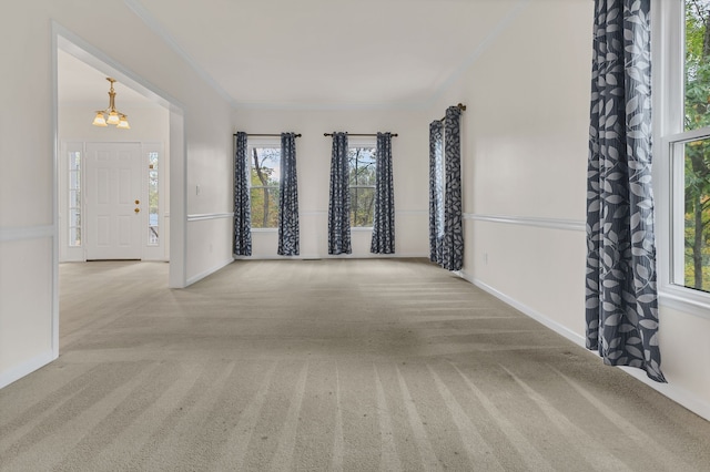 carpeted spare room featuring ornamental molding, a wealth of natural light, and an inviting chandelier