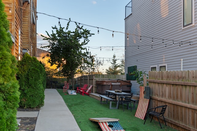 yard at dusk featuring a hot tub and a patio area