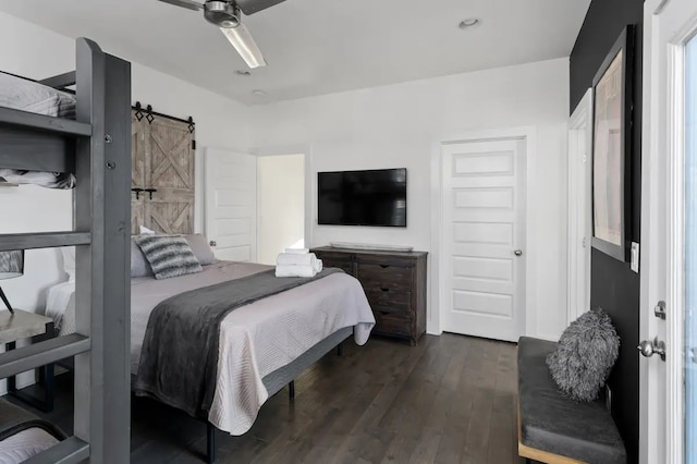 bedroom with a barn door, ceiling fan, and dark hardwood / wood-style floors