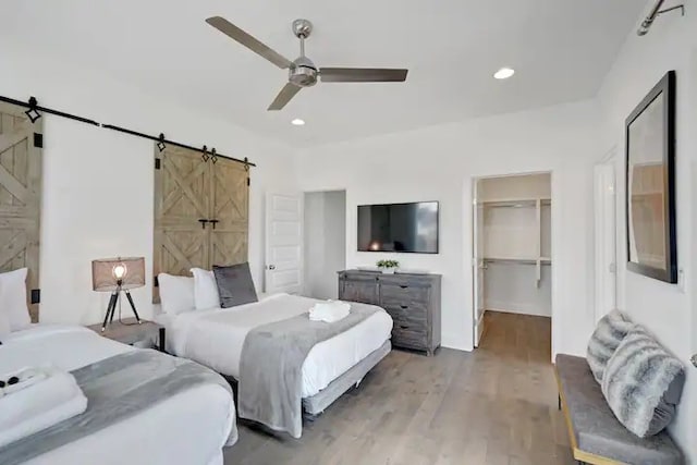 bedroom featuring ceiling fan, light hardwood / wood-style flooring, a walk in closet, a barn door, and a closet