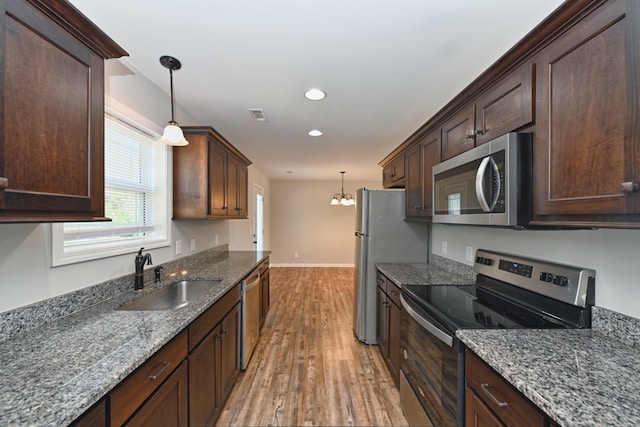 kitchen with light wood-type flooring, sink, decorative light fixtures, and appliances with stainless steel finishes