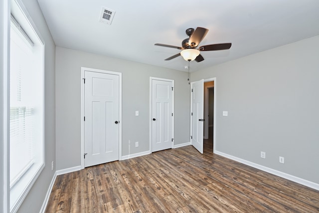 unfurnished bedroom with multiple closets, dark hardwood / wood-style floors, and ceiling fan