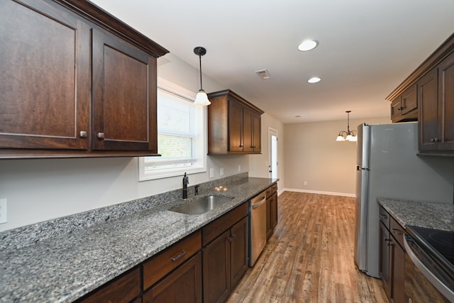 kitchen with stainless steel appliances, dark stone counters, hardwood / wood-style floors, hanging light fixtures, and sink