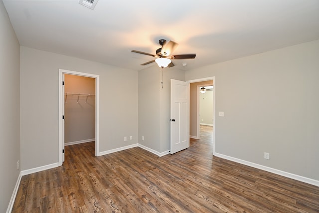 unfurnished bedroom featuring ceiling fan, dark hardwood / wood-style floors, a closet, and a walk in closet