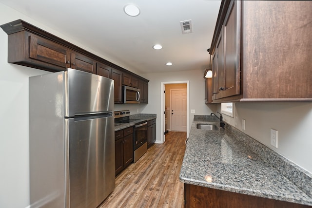 kitchen with stainless steel appliances, light hardwood / wood-style floors, dark stone counters, sink, and dark brown cabinets