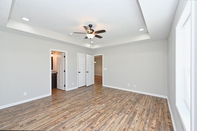 unfurnished bedroom featuring dark wood-type flooring, ceiling fan, connected bathroom, and a raised ceiling