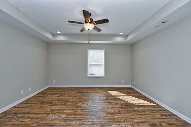 unfurnished room featuring dark wood-type flooring, a tray ceiling, and ceiling fan