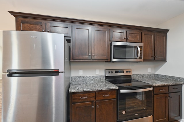 kitchen with dark brown cabinetry, stainless steel appliances, and dark stone countertops