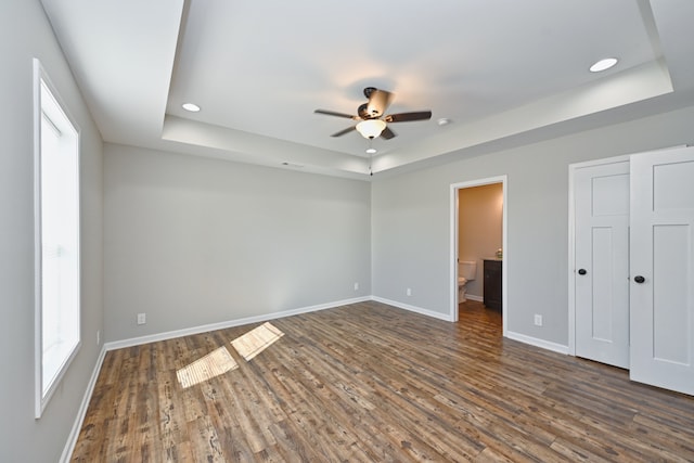 unfurnished bedroom featuring ensuite bathroom, dark hardwood / wood-style floors, ceiling fan, and a tray ceiling