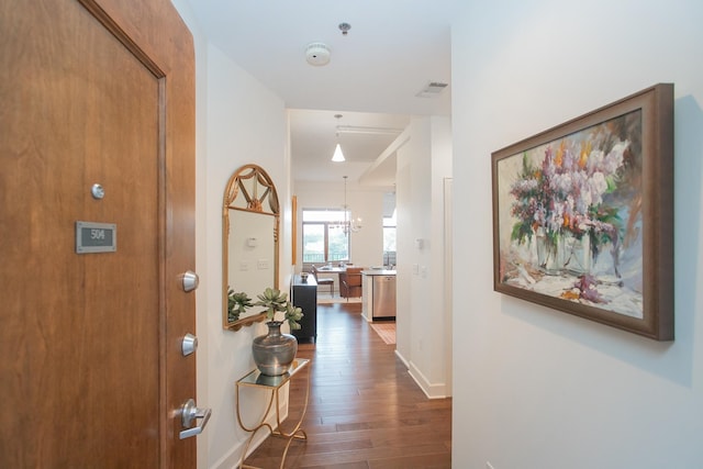 hallway with dark wood-type flooring and a notable chandelier