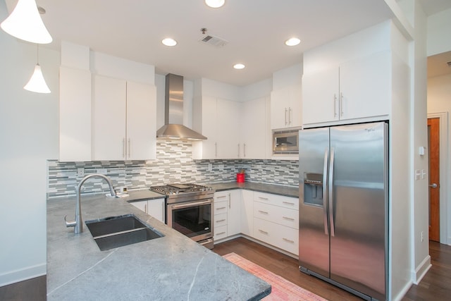 kitchen with appliances with stainless steel finishes, decorative light fixtures, sink, white cabinets, and wall chimney exhaust hood