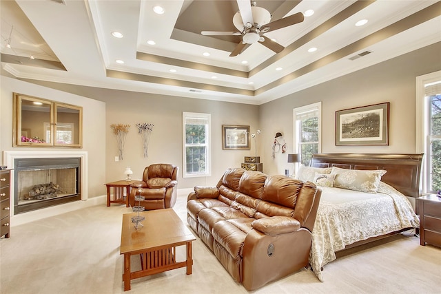 carpeted bedroom featuring crown molding, multiple windows, ceiling fan, and a tray ceiling