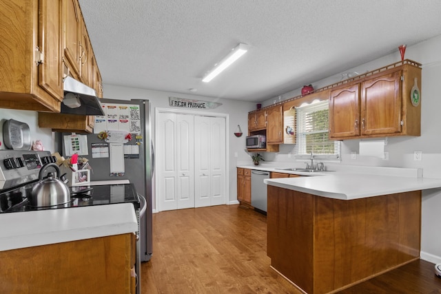 kitchen with sink, kitchen peninsula, appliances with stainless steel finishes, a textured ceiling, and light hardwood / wood-style flooring